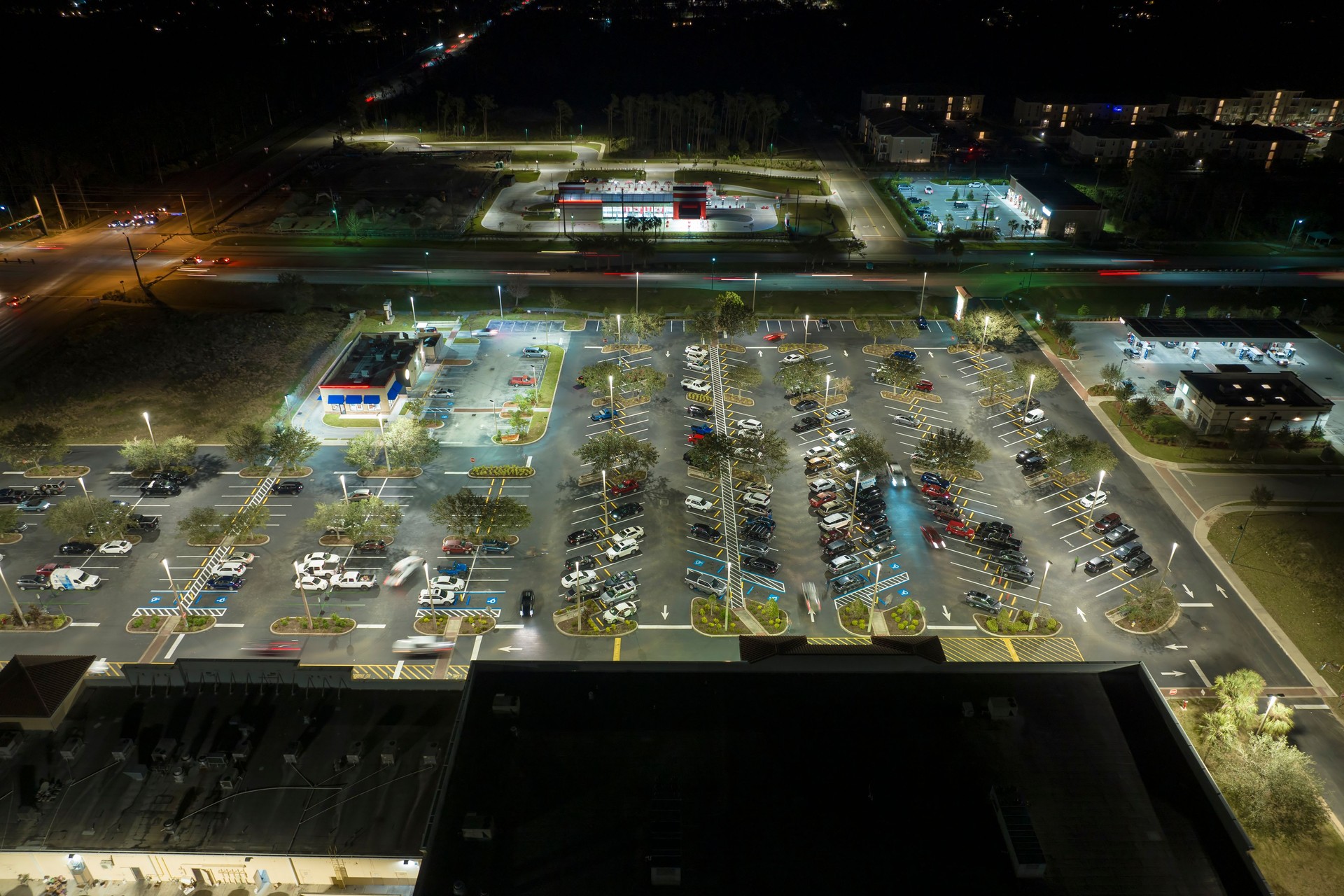 Aerial night view of many cars parked on parking lot with lines and markings for parking places and directions. Place for vehicles in front of a grocery mall store